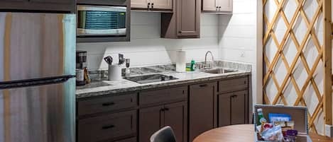 Una cocina equipada con refrigerador, microondas, pileta y alacenas. Hay una mesa de comedor con sillas y una mesita con aperitivos.