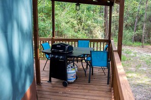 A wooden deck with a grill and chairs, surrounded by trees.
