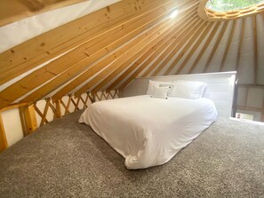 Un dormitori amb un llit, una finestra i estructura de sostre de fusta.