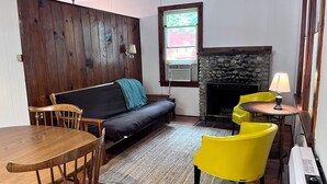 Een gezellige woonkamer met een houten lambrisering, een bank, een eettafel met stoelen, een open haard en een raam met uitzicht.