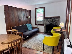 Una sala de estar acogedora con un panel de pared de madera, un sofá, una mesa de comedor con sillas, una chimenea y una ventana con vistas.