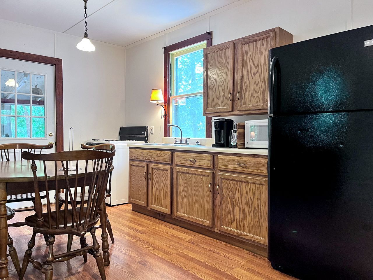 Una cocina con armarios de madera, un refrigerador negro, un microondas y una mesa de comedor con sillas.