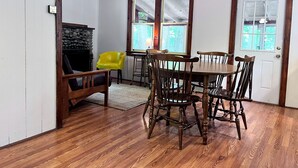 Een eetgedeelte met een houten tafel en stoelen, een gele stoel en een open haard.