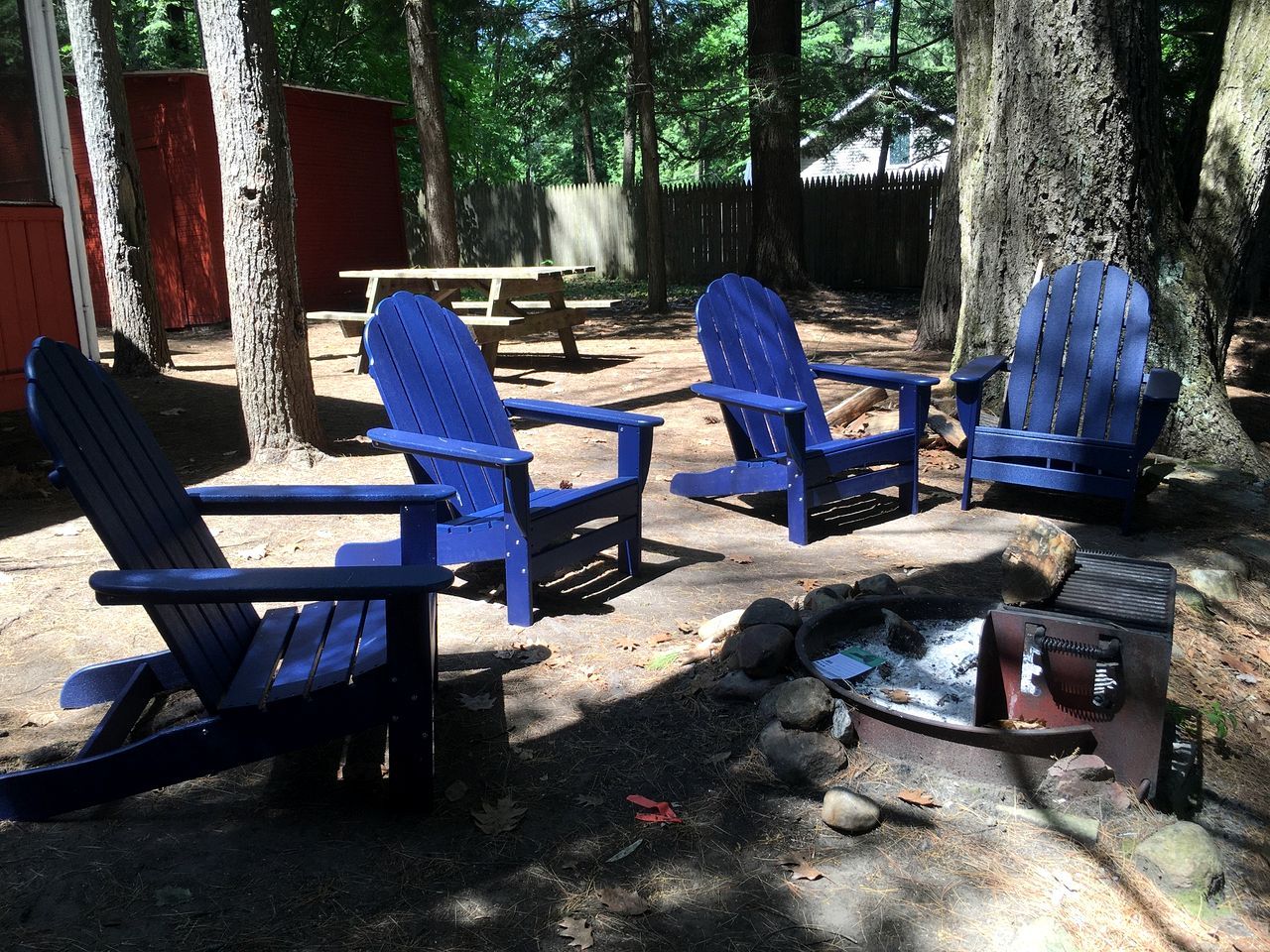 Un camping con cuatro sillas Adirondack azules, una mesa de picnic y una fogata.