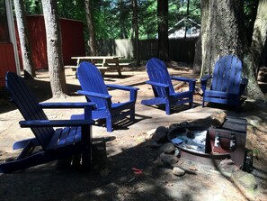 A campsite with four blue Adirondack chairs, a picnic table, and a fire pit.