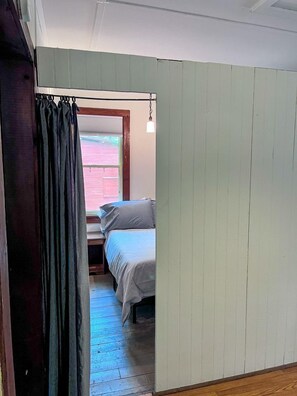 Un pasillo estrecho que conduce a un dormitorio con cama, ventana y lámpara colgante.