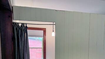 A narrow hallway leading to a bedroom with a bed, a window, and a hanging light fixture.