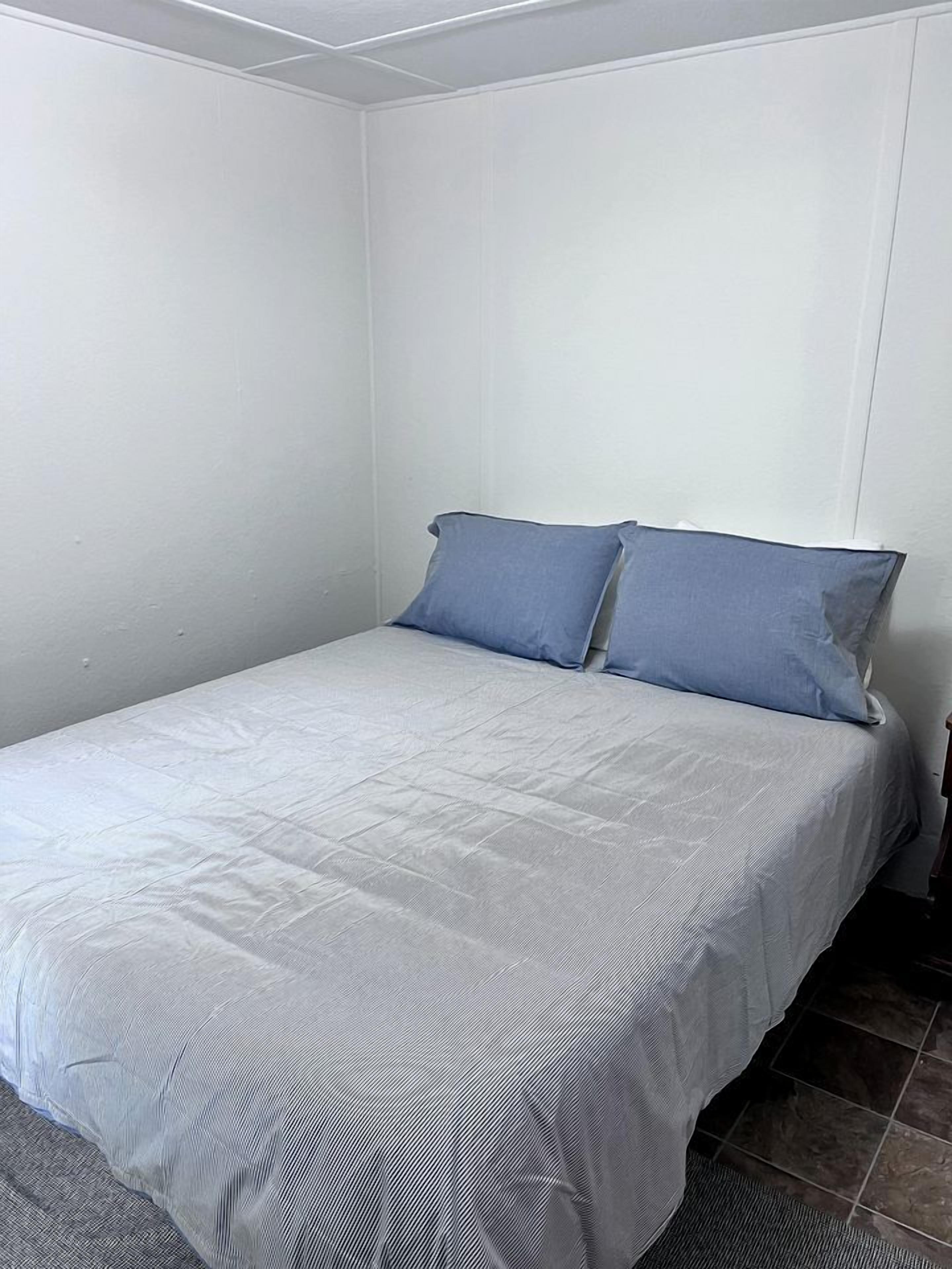 A small, single-bed room with a plain white wall and a dark floor.
