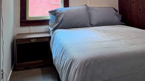 Een slaapkamer met een bed, een raam met zonwering, een nachtkastje en een lamp.