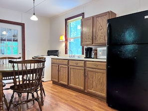 Une cuisine avec des meubles de rangement en bois, un réfrigérateur noir, un four à micro-ondes et une table à manger avec des chaises.