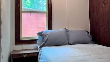 Une chambre à coucher avec un lit, une fenêtre avec des stores, une table de chevet et une lampe.