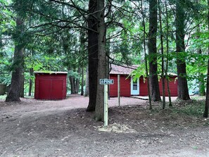 Zona boscosa con edificios rojos, un poste con el rótulo 'PINE' y un sendero de tierra.