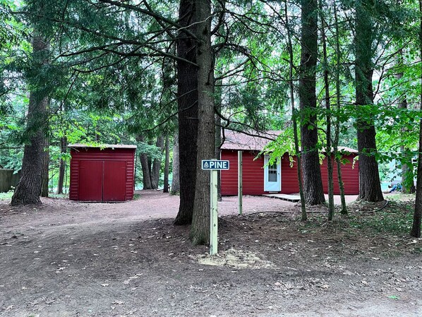 A forested area with red buildings, a signpost labeled 'PINE,' and a dirt path.