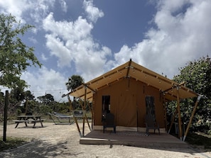 A tented structure with a picnic table and chairs, surrounded by trees and a clear sky.