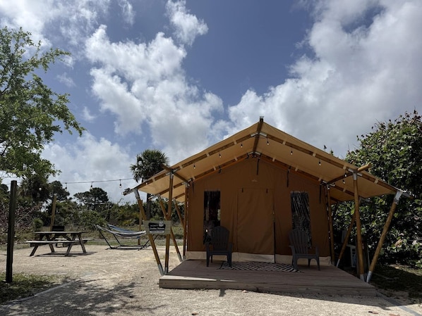 Estructura cubierta con mesa de picnic y sillas, rodeada de árboles y un cielo despejado.