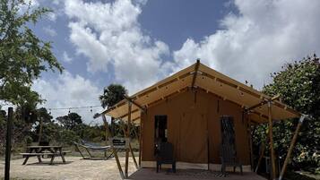 A tented structure with a picnic table and chairs, surrounded by trees and a clear sky.