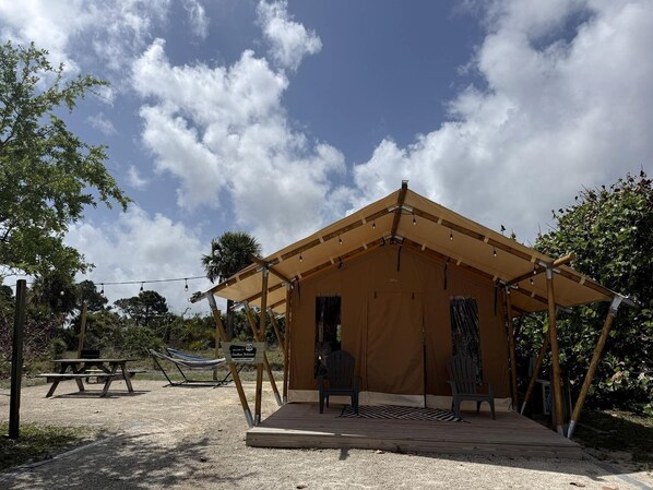 A tented structure with a picnic table and chairs, surrounded by trees and a clear sky.