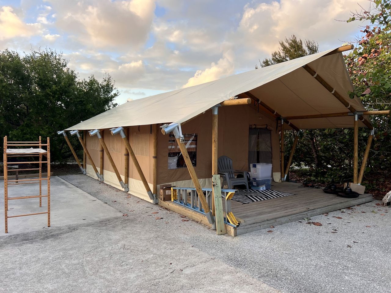 A tent-like structure with a covered porch, a ladder, and a chair.