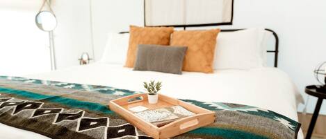 Un lit bien fait, avec une couverture à motifs, une petite plante et un plateau sur lequel sont posés divers objets.