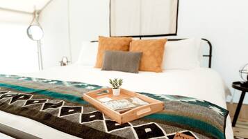 A neatly made bed with a patterned blanket, a small plant, and a tray with items on it.