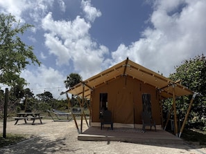 A tented structure with a picnic table and chairs, surrounded by trees and a clear sky.