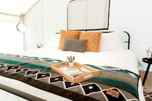 Una cama bien hecha con un edredón estampado, una planta pequeña y una bandeja con objetos encima.