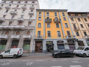 Straßenansicht mit einer Reihe mehrstöckiger Gebäude, darunter ein gelbes Gebäude mit einer Schaufensterfront.