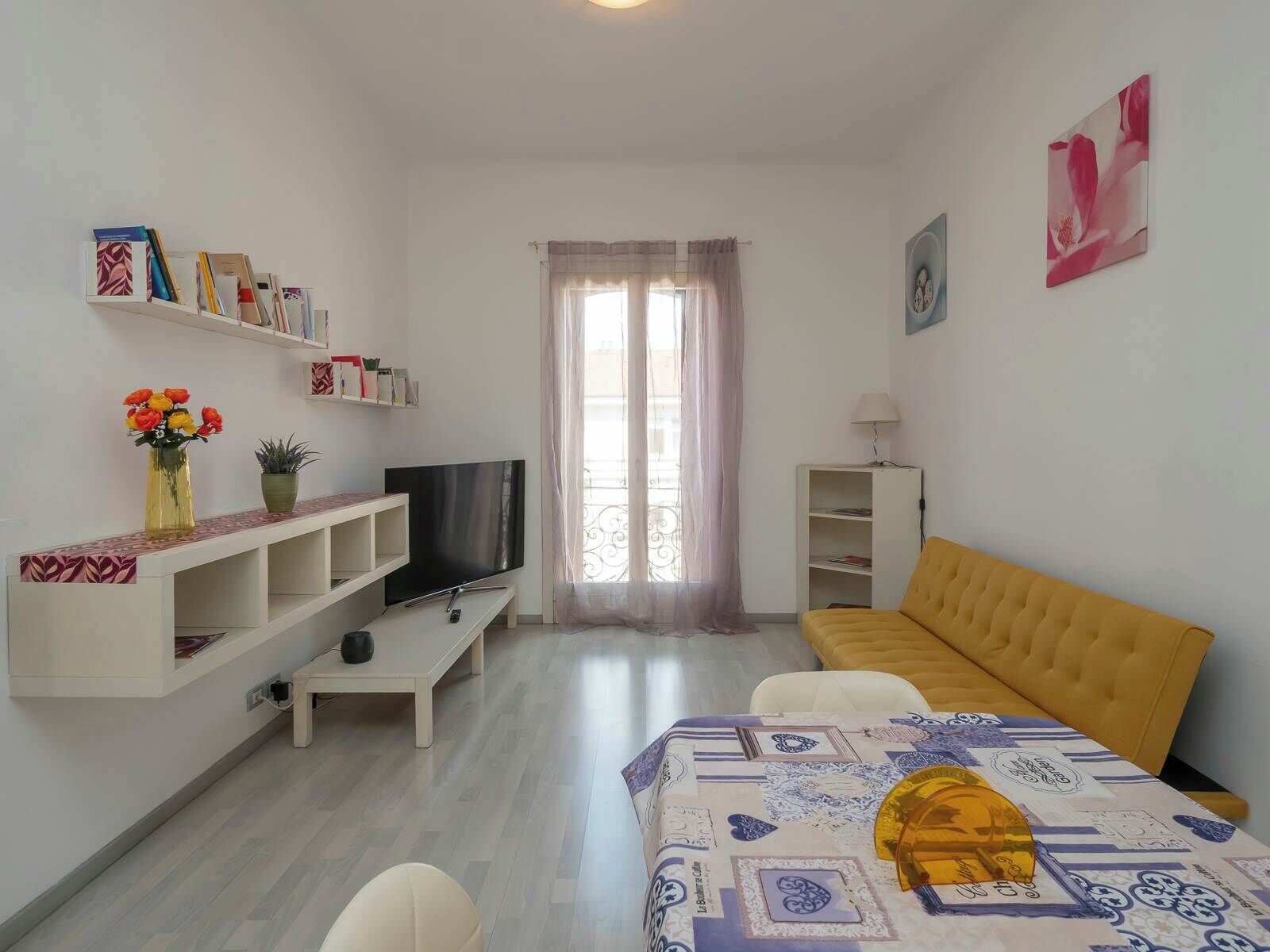 A living room with a sofa, TV, shelves, and a window with curtains.