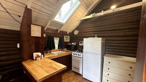 Una cucina in legno tipica di una baita, con un piano di lavoro in legno, un fornello, un frigorifero e un lucernario.