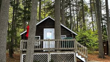 A cabin with a wooden deck, a door, and a staircase leading up to it.