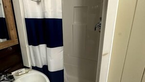 Un bagno con un lavandino bianco, una doccia con sportello bianco e un tenda da doccia a righe blu e bianche.
