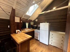 Cocina de cabaña de troncos con encimera de madera, estufa, refrigerador y tragaluz.