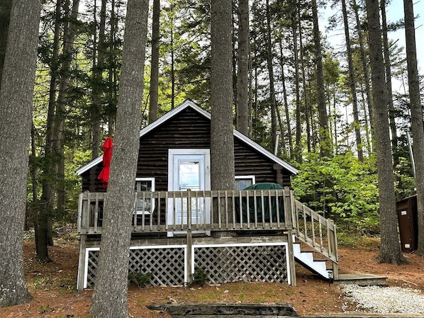 A cabin with a wooden deck, a door, and a staircase leading up to it.