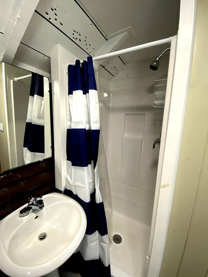 Un baño con un lavamanos blanco, una ducha con puerta blanca y una cortina de ducha azul y blanca.