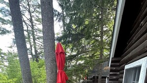 Un pontile in legno con un tavolo e sedie, un ombrellone rosso e un edificio in stile baita.