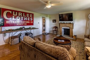 A living room with a fireplace, a television, and a large sign for Curlee Clothes. - Peaceful and Serene Farmstead Retreat with Horseback Riding in Stockton, Illinois, Perfect for a Family Getaway (Stockton)