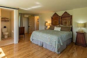 A bedroom with a wooden bed, a nightstand, a bedside table, a lamp, a wardrobe, and a door leading to another room.