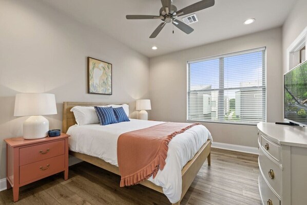 A bedroom with a bed, nightstand, dresser, ceiling fan, window, and artwork.