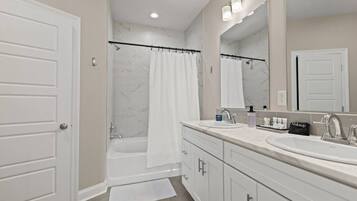 A bathroom with two sinks, a bathtub, a shower curtain, and a large mirror.