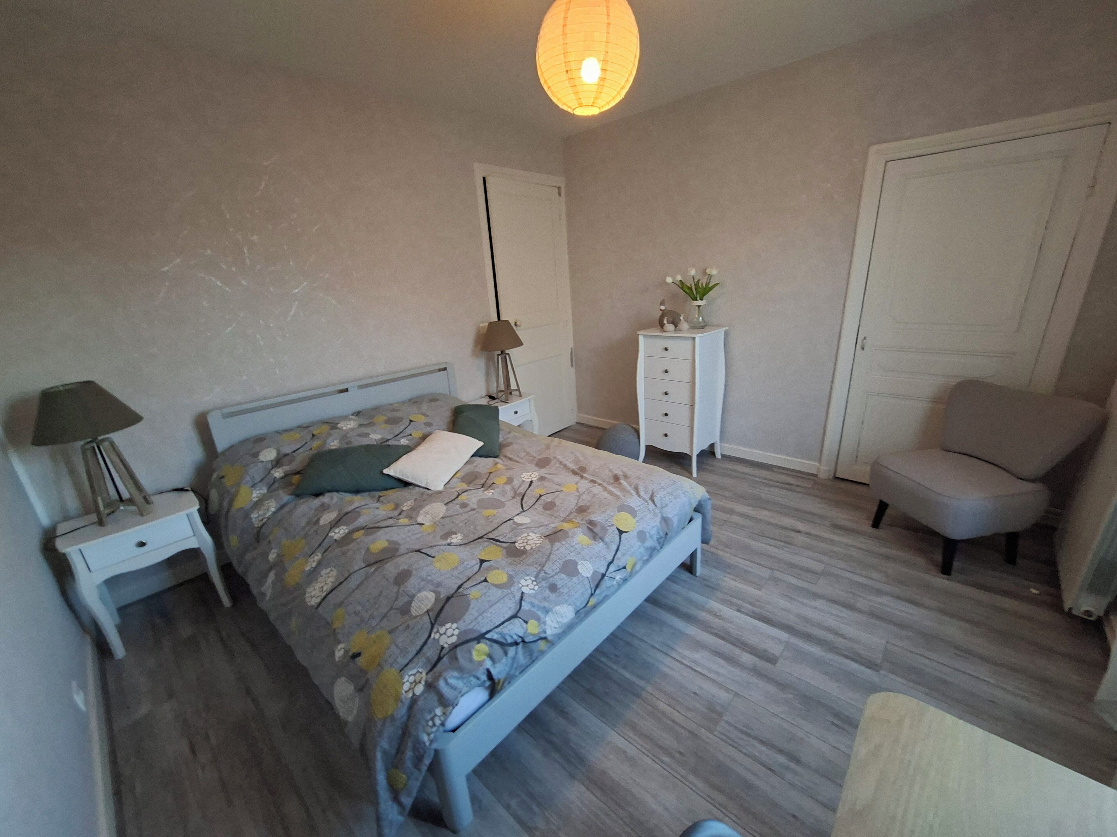 Een slaapkamer met een bed, nachtkastjes, een dressoir, een stoel en een lamp.