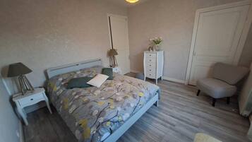 Een slaapkamer met een bed, nachtkastjes, een dressoir, een stoel en een lamp.