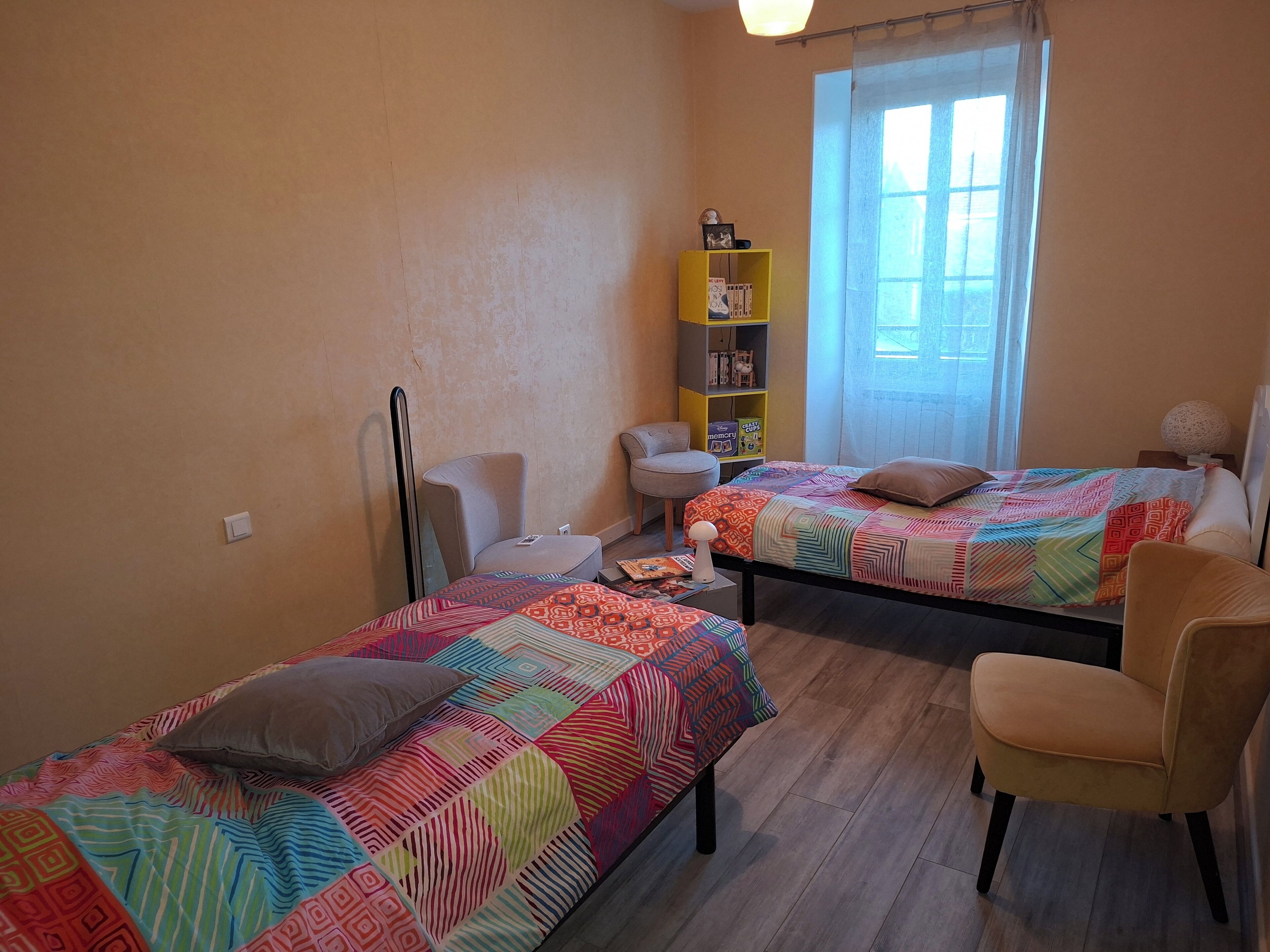 Une chambre avec deux lits, une chaise, une bibliothèque et une fenêtre.
