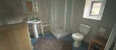 Une salle de bain équipée d’une douche, de toilettes, d’un lavabo et d’un petit tabouret en bois.