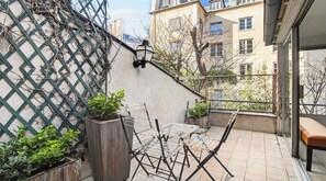 A balcony with a lattice wall, a folding table, chairs, and potted plants. - Luxury Paris Penthouse with Panoramic Rooftop Views | Saint-Germain (Paris)