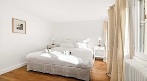 A bedroom with a bed, bedside tables, lamps, a radiator, and a window with curtains. - Luxury Paris Penthouse with Panoramic Rooftop Views | Saint-Germain (Paris)