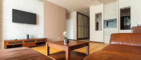 A modern living room with a flat-screen TV mounted on a textured wall, a wooden coffee table, and a brown leather sofa.