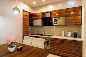 Cocina compacta con armarios de madera, horno empotrado, cafetera y comedor con mesa y sillas.