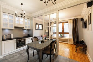 A modern kitchen with a dining area, featuring a large window, a chandelier, and a flat-screen TV. - Aapartments - Ideal City Center Location (Warszawa)