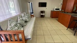 A room with a sofa, a television, a microwave, and a kitchen area.