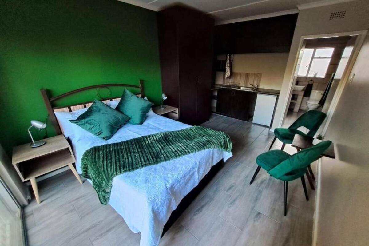 Ein Schlafzimmer mit einem Bett, grünen Stühlen, einem Nachttisch und einer kleinen Küche im Hintergrund.